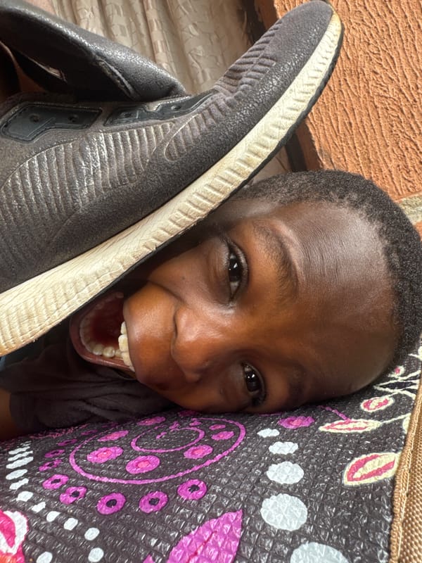 Child on patterned mat, sneaker near face, Onitsha