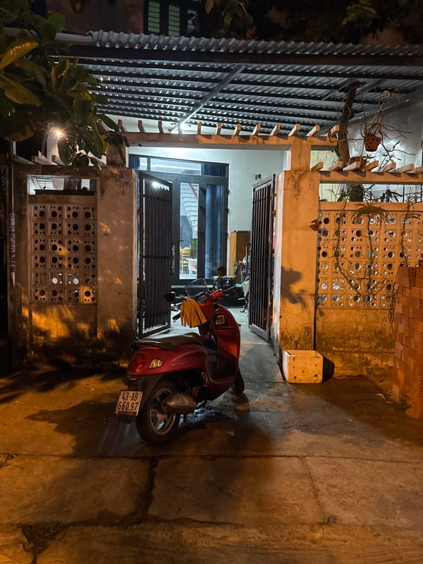 Red scooter parked in worn Đà Nẵng alleyway at night