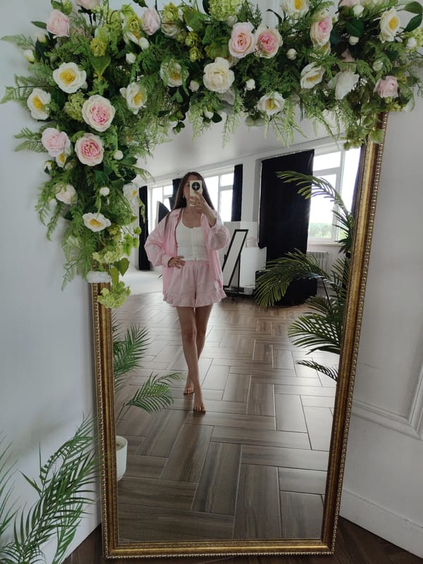 Woman takes mirror selfies in pink outfit, floral decorated room
