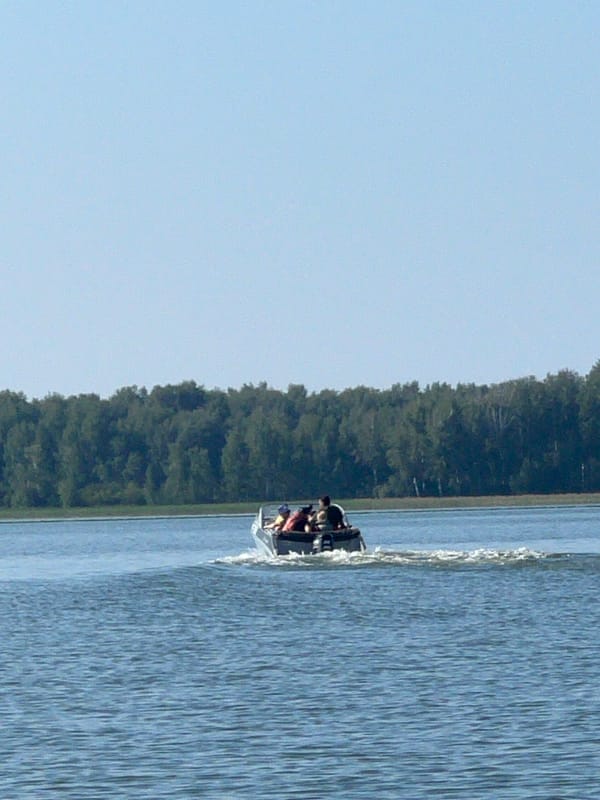 Motorboat crossing calm Russian lake near wooded shoreline
