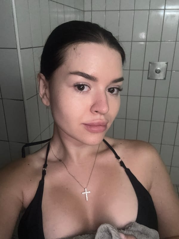 Indoor close-up in a Prague bathroom, black bikini and cross necklace.