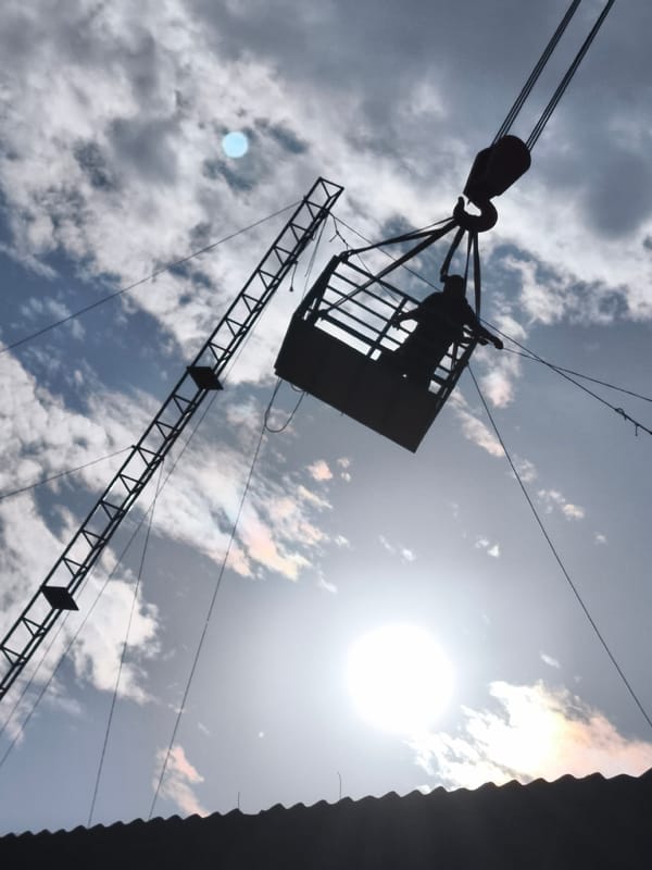 Crane lifts two people in basket above Chimbote rooftops