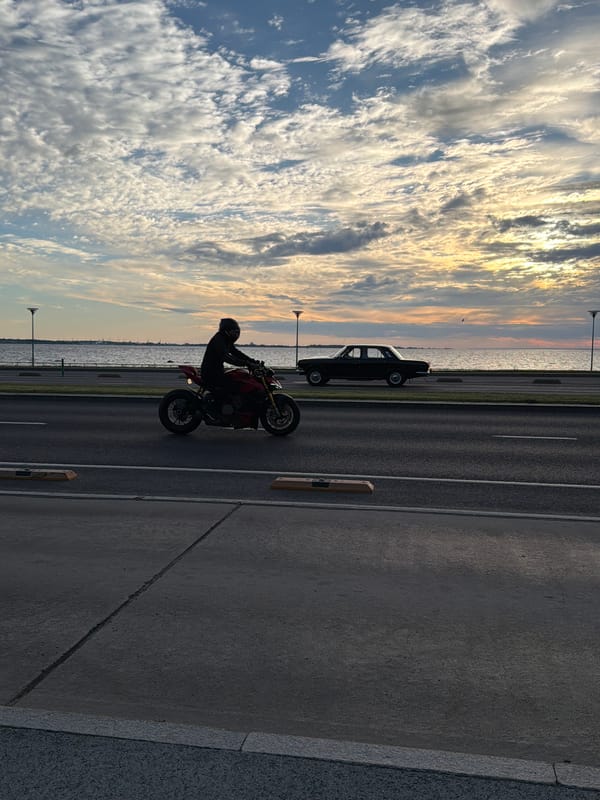 Motorcycle and vintage car silhouetted on Tallinn's coastal road at sunset