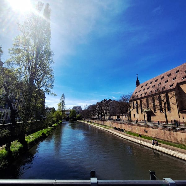 Pedestrians stroll along Strasbourg canal under clear skies