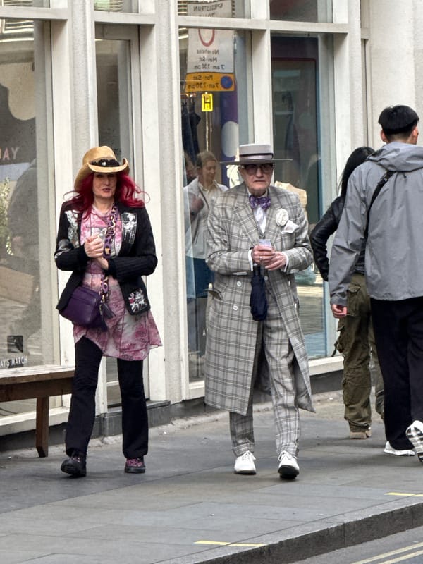 Pedestrians walk London sidewalk, man carries rubbish bags