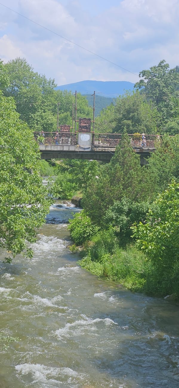 People cross old iron bridge over rushing river