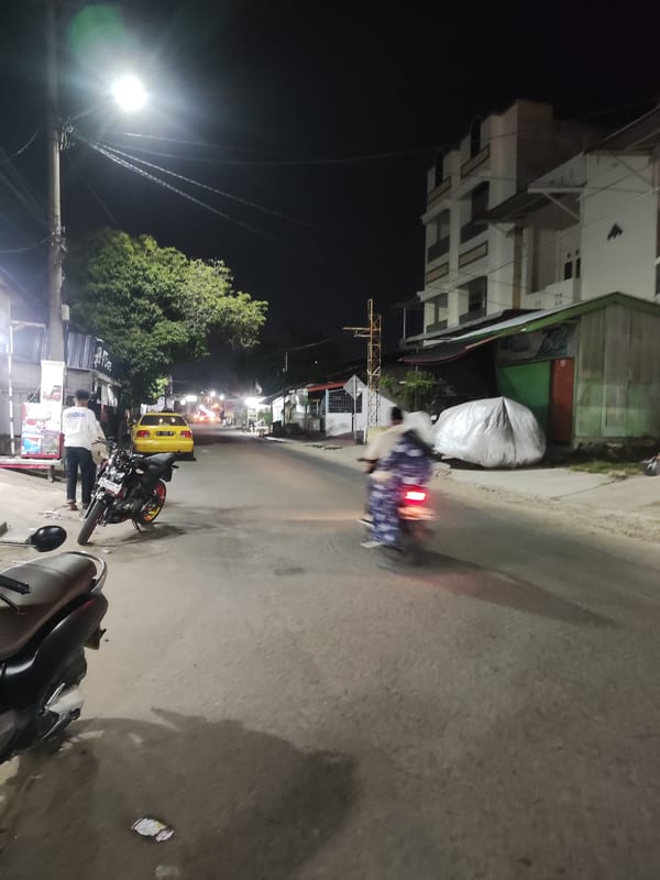 Man stands beside motorcycle on lit Lhokseumawe street