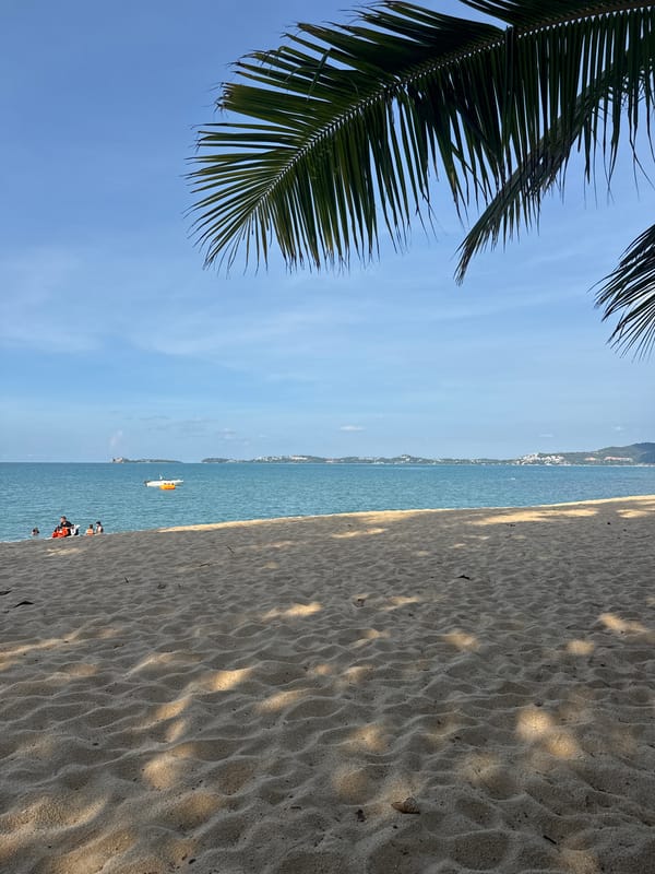 Sunny morning on a Ko Samui beach with boats and beachgoers
