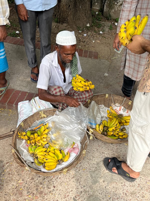 Elderly banana vendor sits at morning marketplace in Dhaka