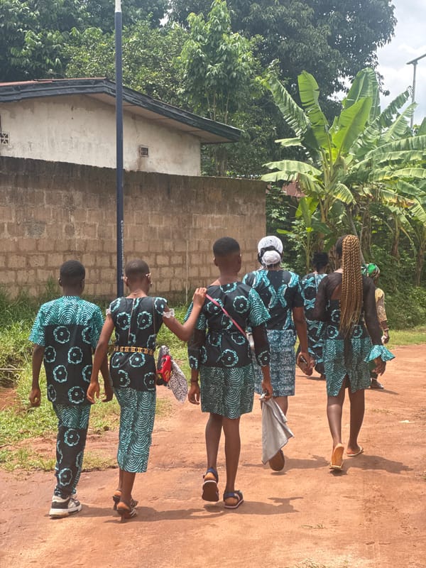 Five women in matching dresses walk through Eziudo, Nigeria