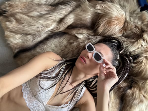 Woman in sunglasses and lace top observed on fur rug