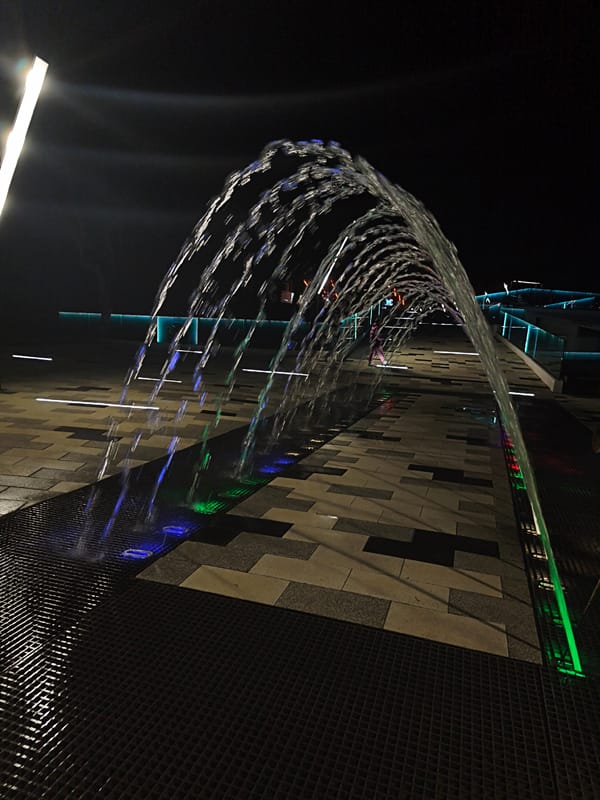 Evening visitors experience illuminated fountain walkway in Russian coastal cities