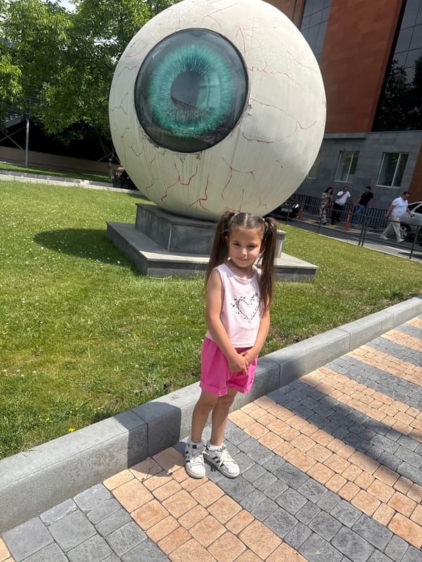 Girl poses with large eyeball sculpture in urban setting