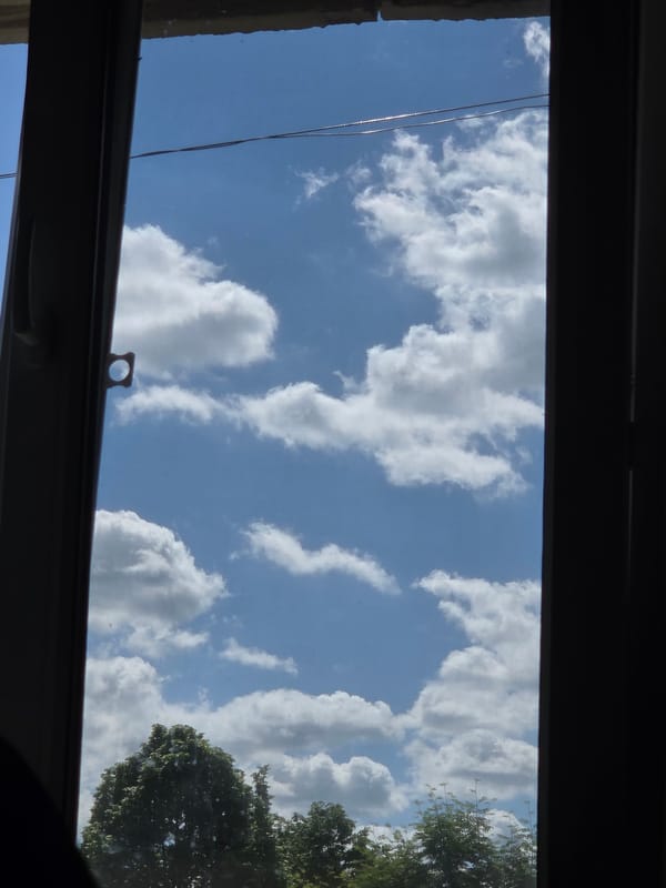 Sky view captured through window frame shows clouds, tree