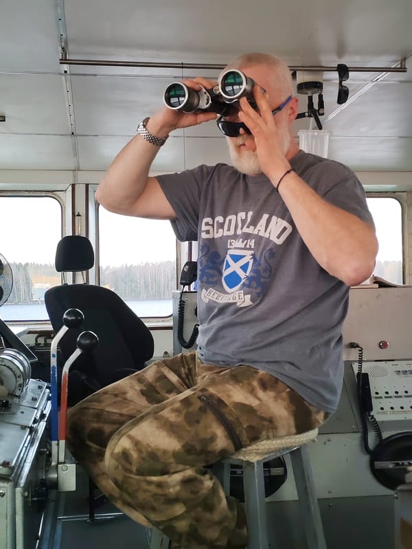 Man in Scotland shirt uses binoculars aboard vessel near Anisimovo