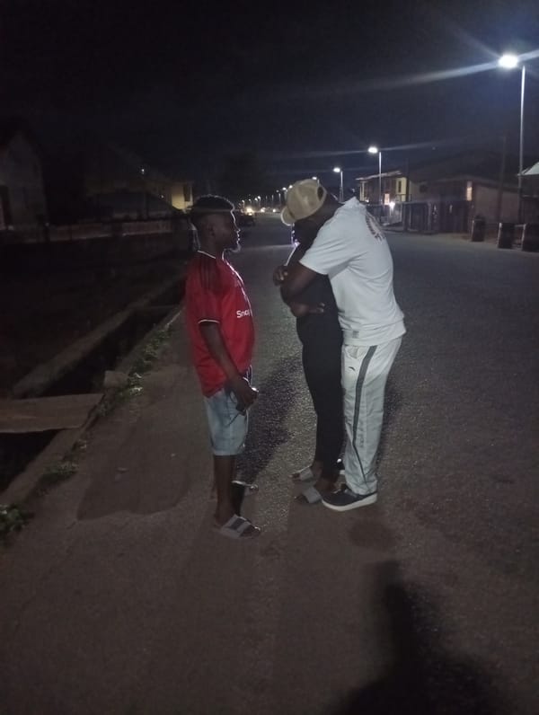 Two people interact on nighttime street in Jos, Nigeria