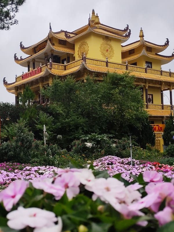 Yellow Buddhist temple photographed through flower gardens in Da Lat
