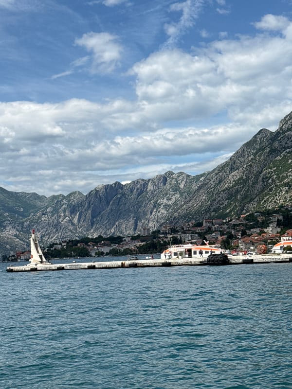 Crowds gather at Kotor harbor pier amid mountain backdrop