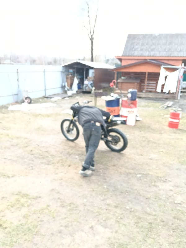 Person services motorcycle in Russian village yard