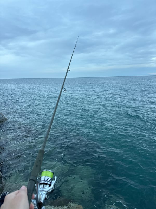 Morning angler fishes from rocks in Greek coastal town