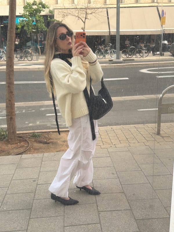 Woman reflected in Tel Aviv storefront window while using phone