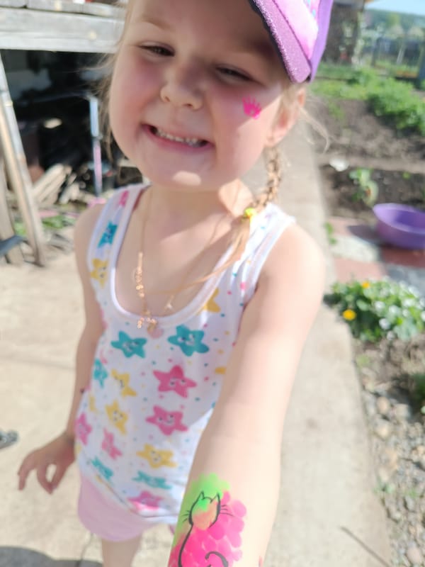 Girl with pink crown, cat face paint smiles for camera