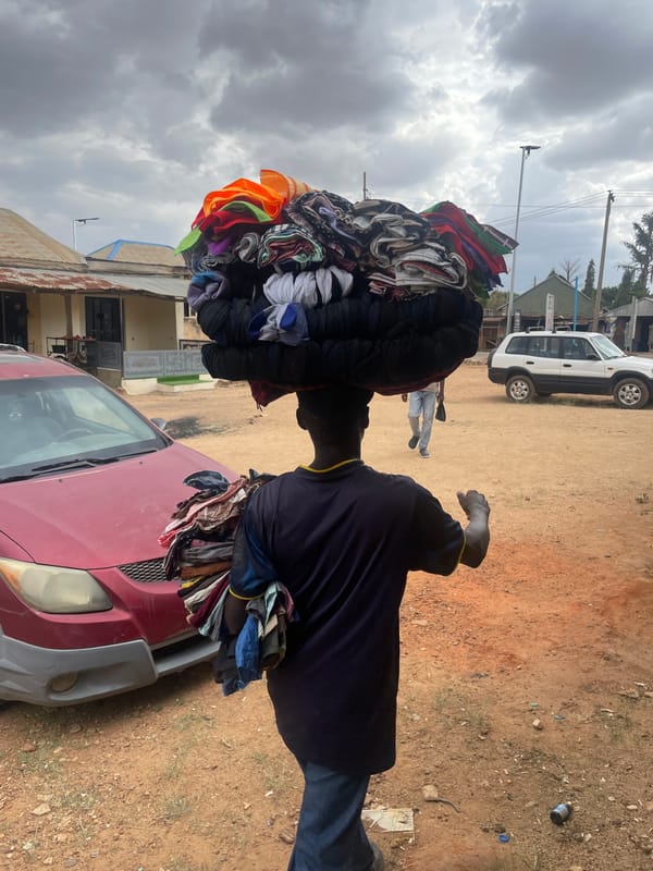 Street vendor carries clothing stack on dirt road in Nigeria