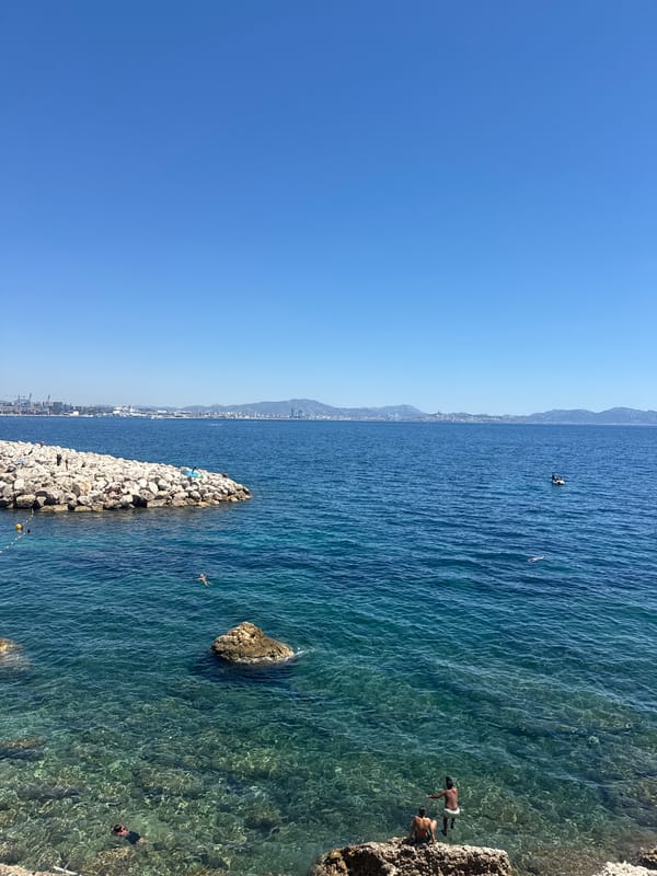 Sunny day along a rocky coastal path near a city.