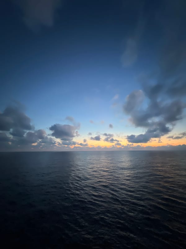 Cargo ship crosses open sea under a twilight sky