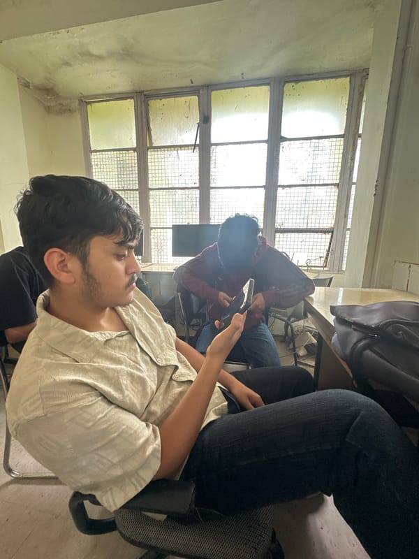 Friends killing time in a classroom, phones out, arm wrestling.