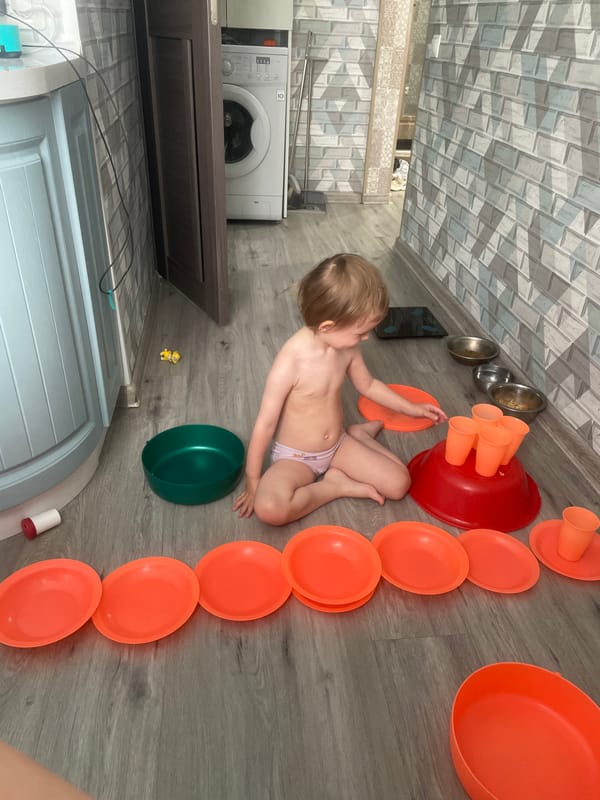 Toddler plays with plastic dishes on floor in Vladivostok