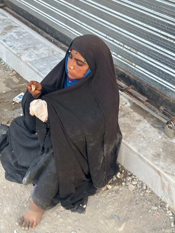 Elderly woman sits on Quetta sidewalk near closed shop