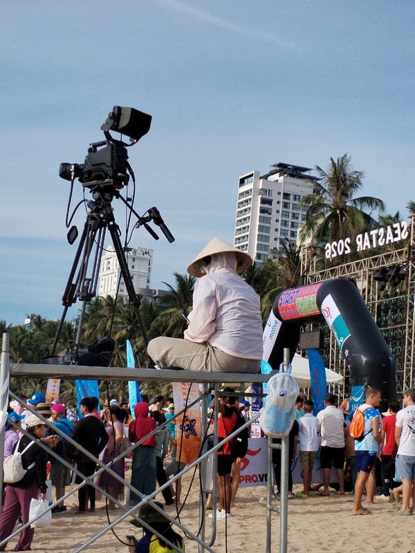 Crowded Nha Trang beach with filming setup and city backdrop