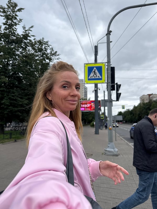Smiling on a Saint Petersburg sidewalk in a pink bomber jacket