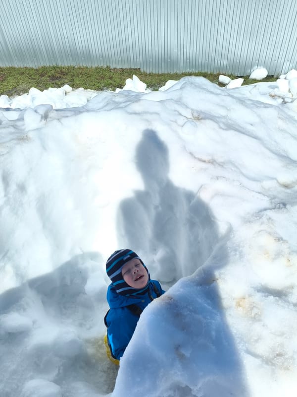 Child plays in snow, woman drinks beverage in Russian village