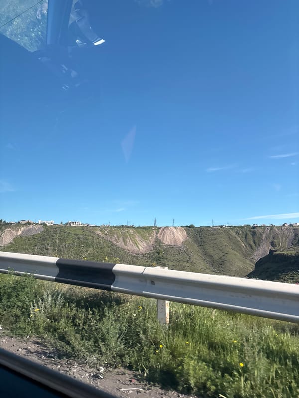 Vehicle travels mountainous road in Kanakeravan, Armenia under clear skies