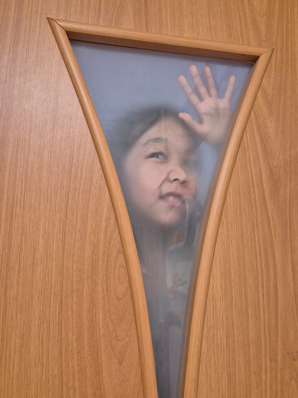 Child plays at door, bun enjoyed in Kokshetau morning
