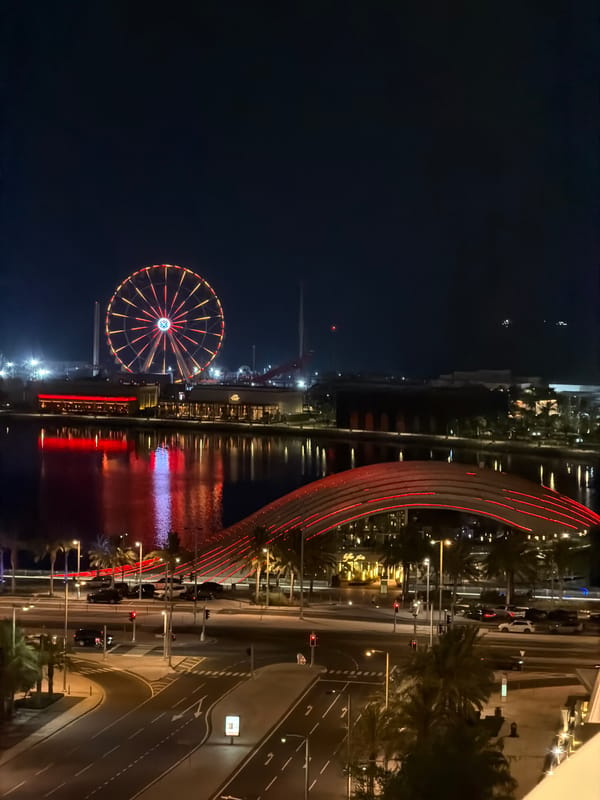 Blue-lit Ferris wheel glows over a city waterfront at night
