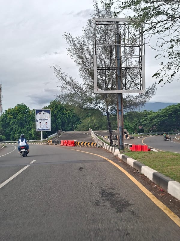 Motorbike rider travels curved road during overcast night in Indonesia