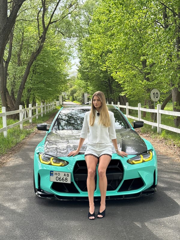 Woman poses with turquoise BMW on tree-lined road