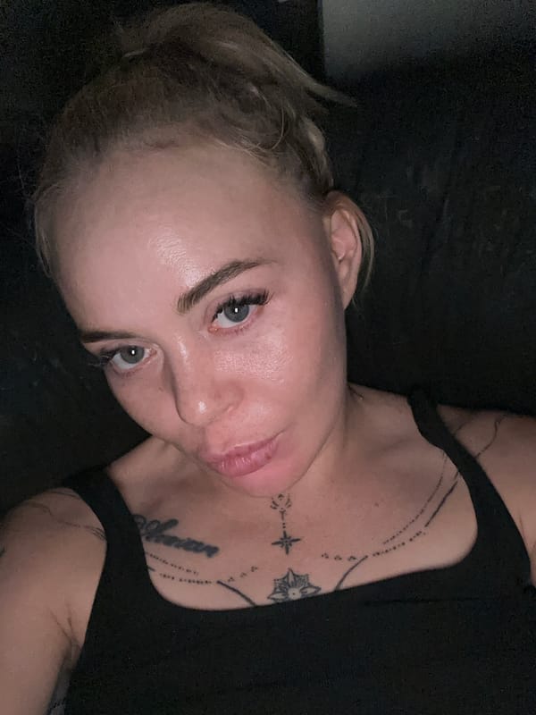Tattooed blonde woman captures multiple selfies in dimly lit setting