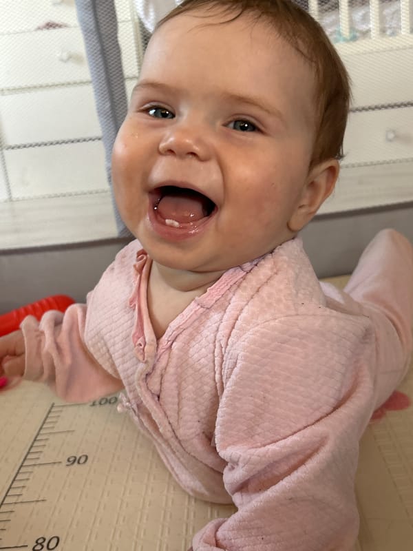 Baby in pink outfit smiles on mat in Rusalevka
