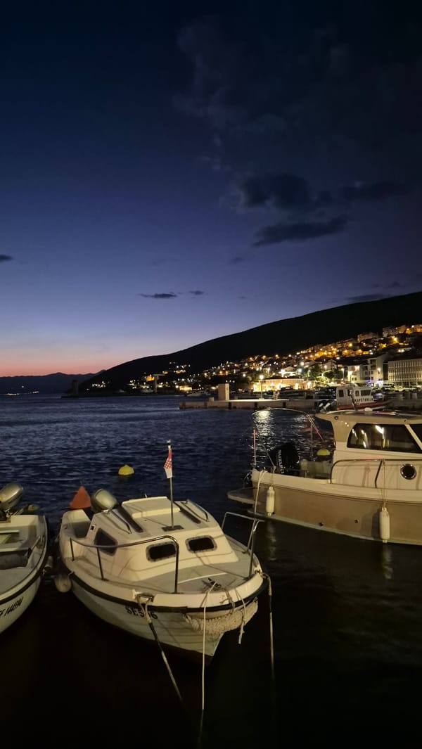 Coastal town harbor at dusk, boats moored, lights coming on