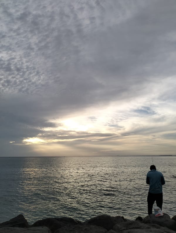 Lone angler fishes from rocky coast during sunset in Lhokseumawe