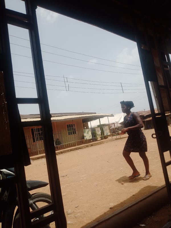 Woman in floral dress walks dirt street past modest buildings