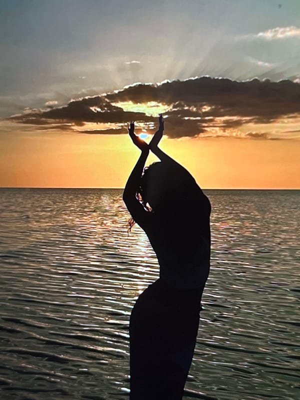 Flowing garment, raised arms, shallow water at sunset