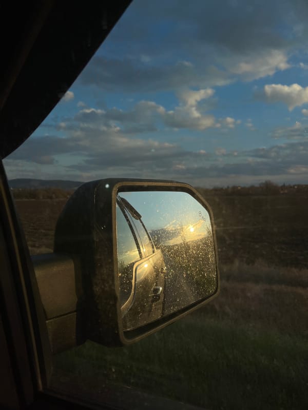 Car mirror reflects cloudy landscape in Bulgarian village