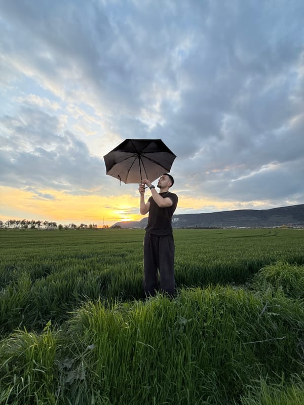 Man with umbrella stands in Bulgarian field at sunset