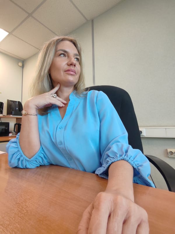 Seated at a wooden desk in a light blue blouse
