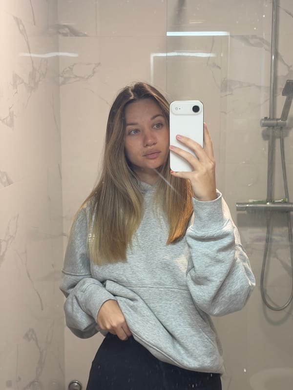 Woman takes bathroom mirror selfie in grey sweatshirt